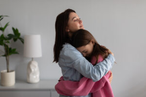 A mom embraces and comforts her daughter, who has experienced chilhdood trauma.