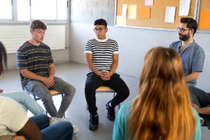 A small group of teens is participating in social anxiety treatment for teens. They're sitting in a circle and talking.