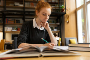 A teen girl, sits at a desk and writes meticulously in her notebook. She is someone who lives with the symptoms of OCD.